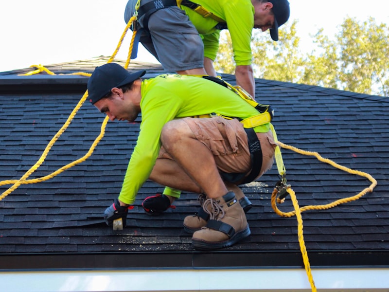 Two roofers in safety harnesses installing shingles on a roof